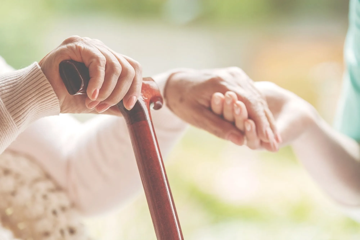 ALLTAGSBEGLEITUNG - Nahaufnahme einer älteren Dame, die in der einen Hand einen Gehstock und in der anderen die Hand der Krankenschwester hält